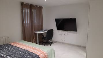 Une chambre à coucher avec un lit, un bureau avec une chaise, une télévision et une fenêtre avec des rideaux.