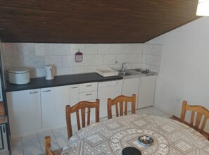 A compact kitchen with white cabinets, a black countertop, a sink, and a stove. There is a dining table with chairs in front. - Apartments Azuro (Dugi Rat)