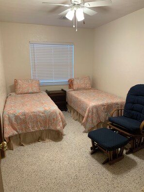 Ein Schlafzimmer mit zwei Einzelbetten, einem Holzstuhl und einem Deckenventilator.