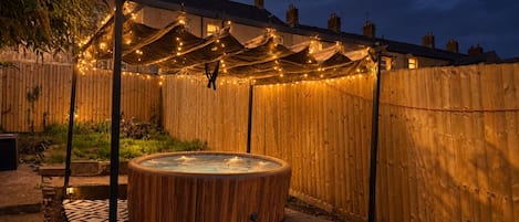 A hot tub in a backyard with string lights and a wooden fence.