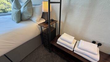A neatly made bed with pillows, a bedside lamp, and a shelf with folded towels.