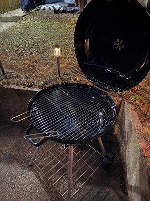 Een zwarte barbecue met een metalen rooster, open deksel en een klein lampje op de grond.