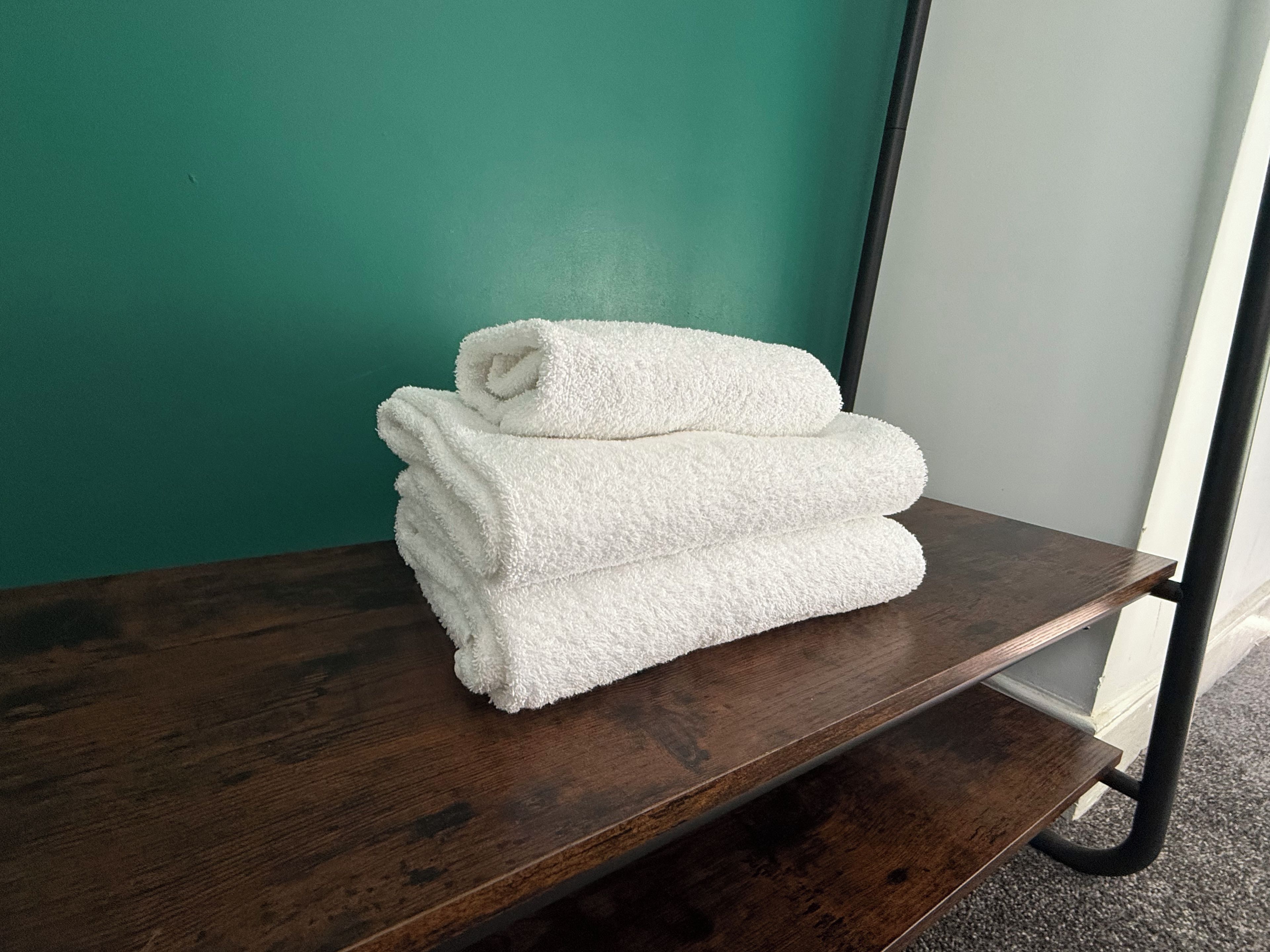 A stack of white towels on a wooden shelf against a teal wall.