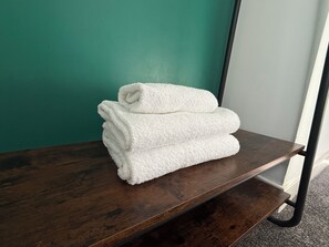 Een stapel witte handdoeken op een houten plank tegen een groenblauwe muur.