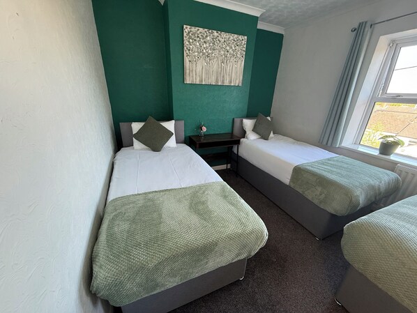 Ein Zimmer mit zwei Einzelbetten, einem kleinen Tisch und einem Fenster mit Vorhängen.