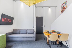 Ein modernes Interieur mit einem grauen Sofa, einem Esstisch mit Stühlen, einer schwarzen Tür und einem an der Wand befestigten Schild mit der Aufschrift 'NETFLIX'.