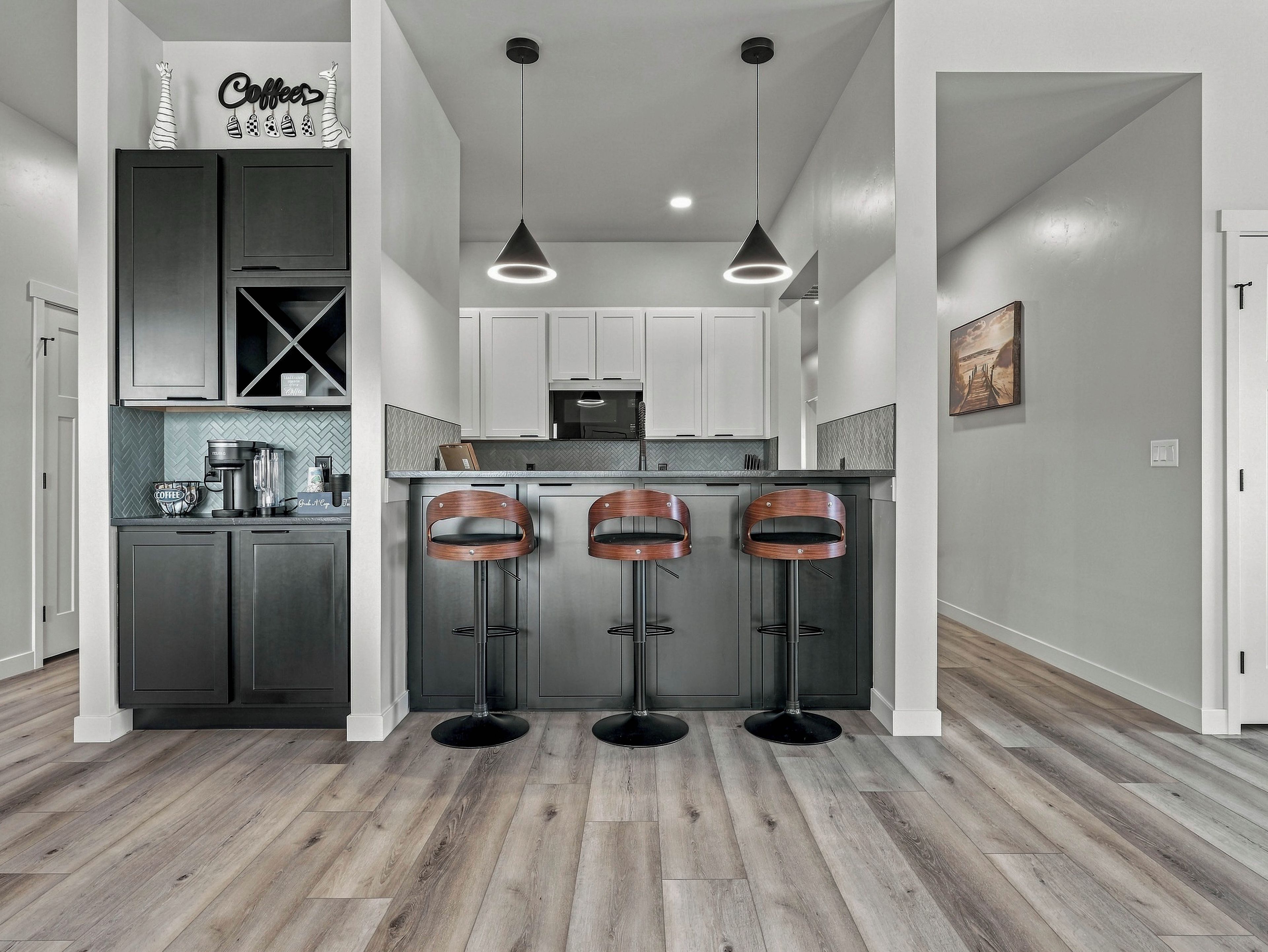 A modern kitchen with dark cabinets, a coffee station, and three bar stools.