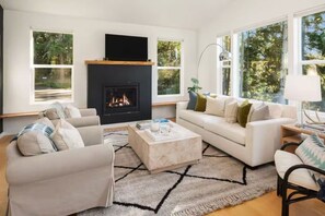 A modern living room with a fireplace, large windows, and a cozy seating arrangement. - Whidbey Island Oasis with Hot Tub and Fire pit (Freeland)