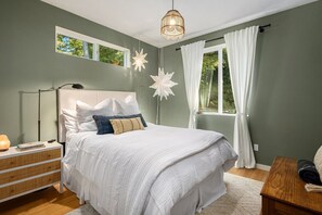 A bedroom with a bed, bedside table, lamp, and a window with curtains. - Whidbey Island Oasis with Hot Tub and Fire pit (Freeland)
