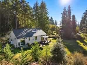 A single-story house with a deck, surrounded by a forested area. - Whidbey Island Oasis with Hot Tub and Fire pit (Freeland)