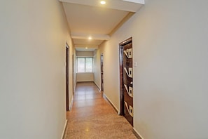 A corridor with a tiled floor, a door with a geometric design, and a window at the end. - Super Townhouse Vaishnavi (Hyderabad)