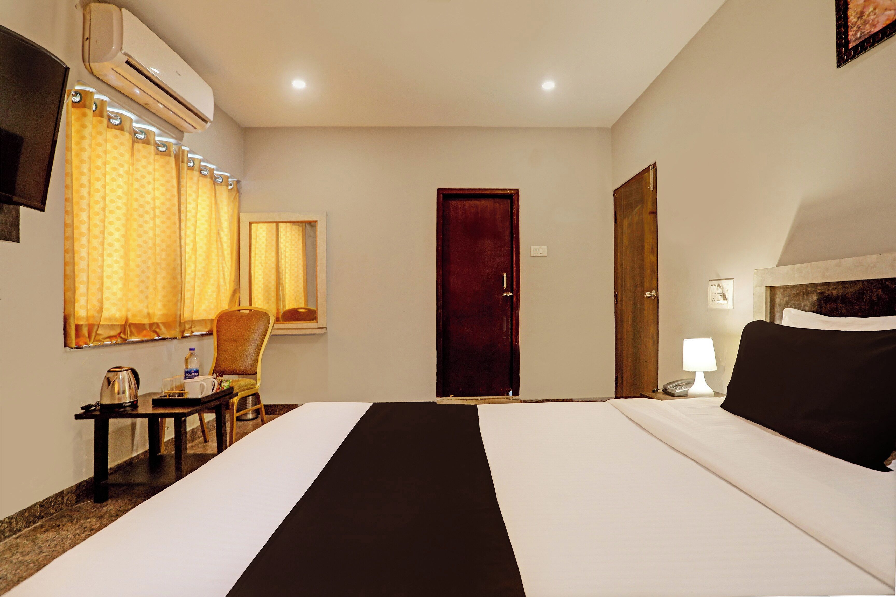 Una habitación de hotel con una cama, una silla, una mesa con hervidor, una lámpara y una puerta.