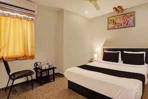 A hotel room with a bed, a chair, a small table with a kettle and cups, a nightstand with a lamp, and a painting on the wall. - Super Townhouse Vaishnavi (Hyderabad)