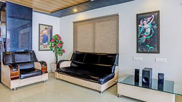 Una sala de estar con un sofá, dos sillones, una mesa de centro de vidrio y dos altavoces fijados a la pared.