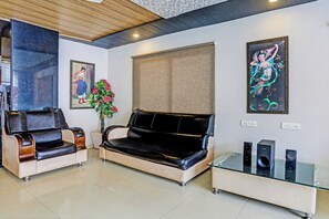 A living room with a sofa, two armchairs, a glass coffee table, and two wall-mounted speakers. - Super Townhouse Vaishnavi (Hyderabad)