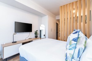 A modern hotel room with a bed, a flat-screen TV mounted on the wall, a wooden desk, and a potted plant. - Newlands Peak Studio with AC (Cape Town)