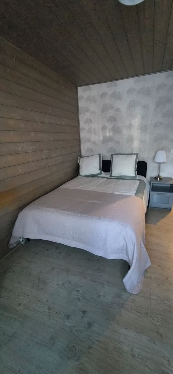 Une chambre avec un plafond en bois, un lit avec une literie blanche, une table de chevet avec une lampe et un mur à motifs.