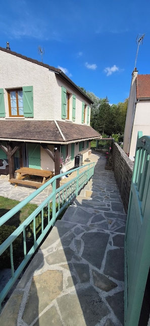 Un sentier pavé de pierres mène à un bâtiment doté d’une terrasse en bois et d’une rambarde verte.