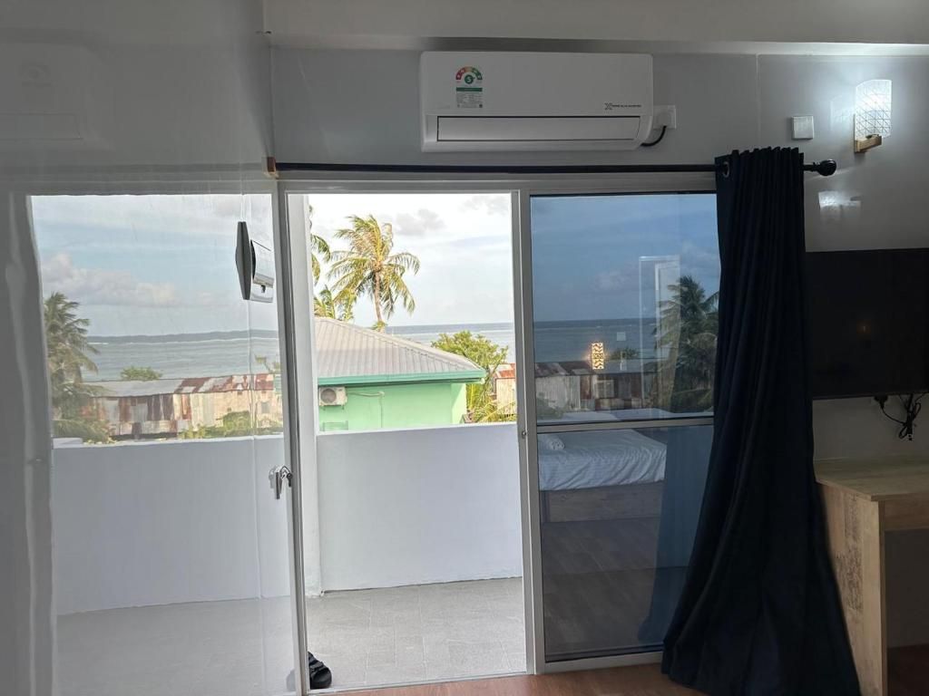 Una habitación con puerta de vidrio corredera que da a un balcón con vistas a palmeras y edificios.