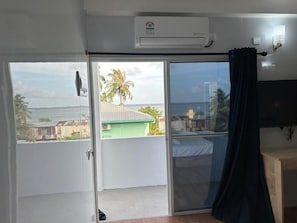 A room with a sliding glass door leading to a balcony with a view of palm trees and buildings. - chao 4p investment guest house  (Maafushi)