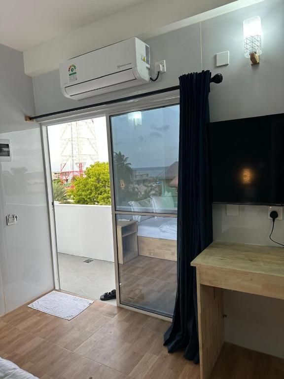 Una habitación con una puerta corrediza de vidrio que da a un balcón, un televisor de pantalla plana montado en la pared y un equipo de aire acondicionado sobre la puerta.