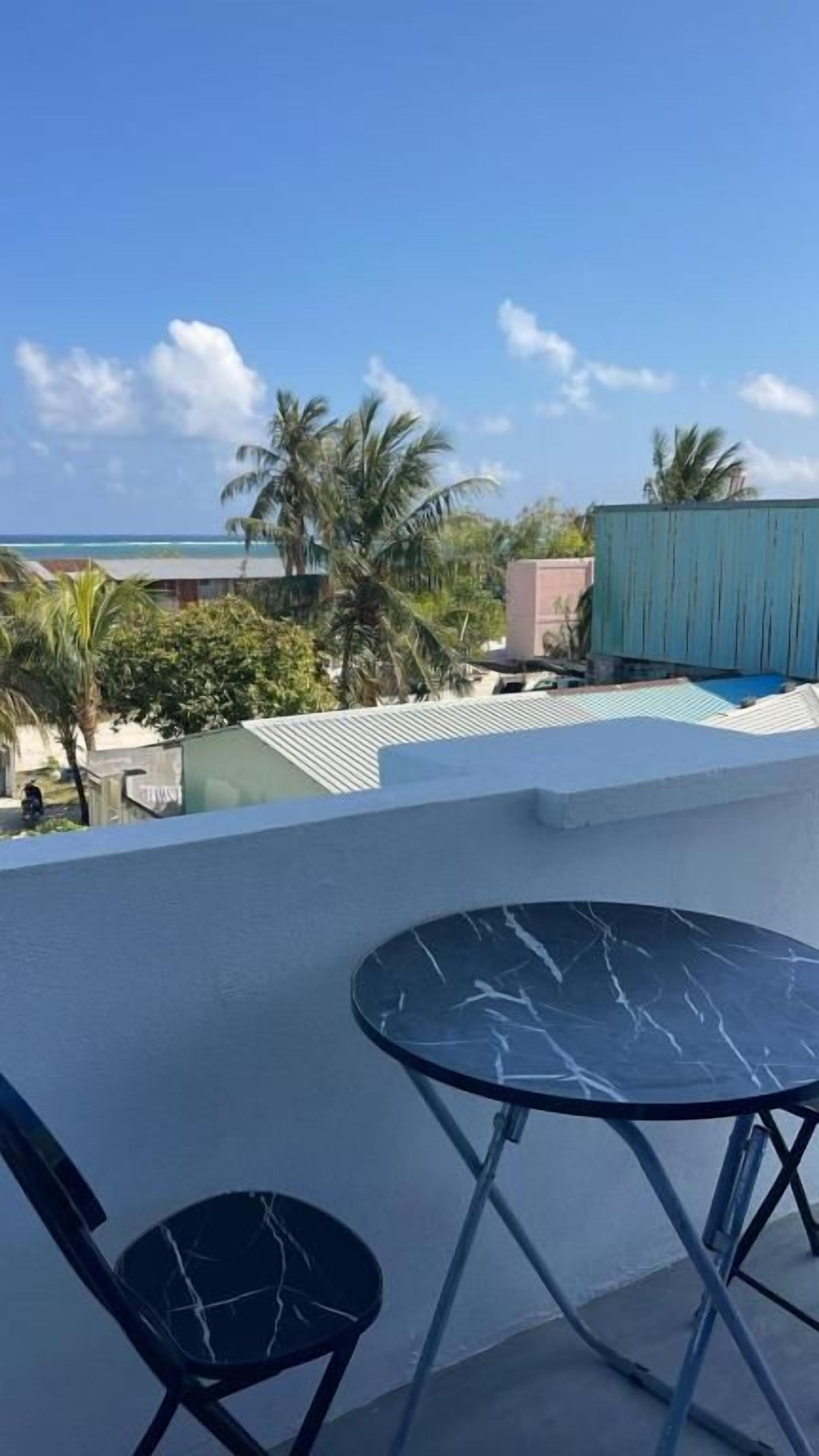 A balcony with a table and chairs, overlooking a beach and palm trees.