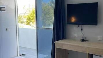 Una habitación moderna con puerta de vidrio corredera que da a un balcón, un televisor de pantalla plana en la pared y un escritorio de madera.