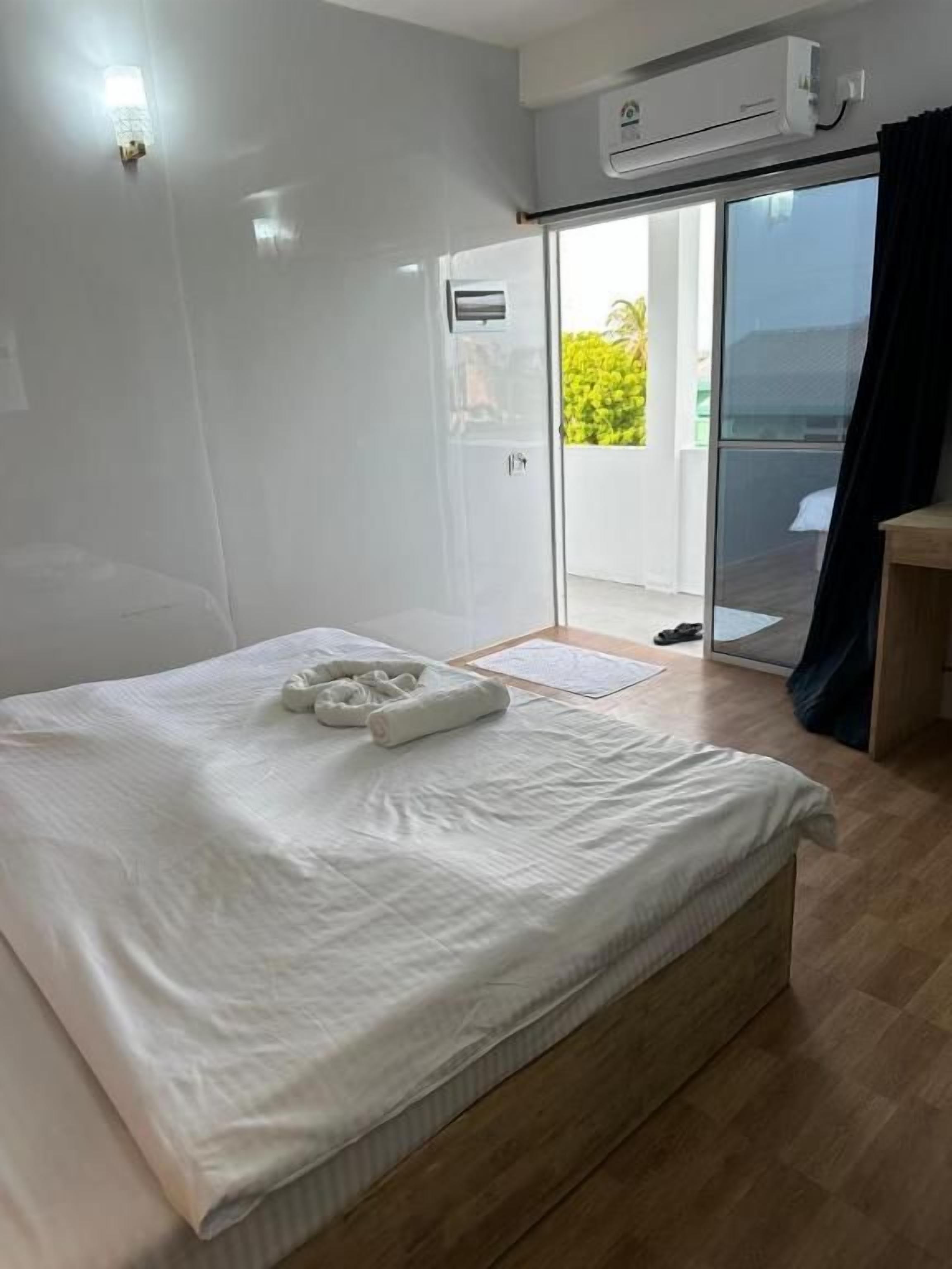 Habitación de hotel con una cama, una mesita, una puerta corrediza de vidrio a un balcón y un equipo de aire acondicionado.