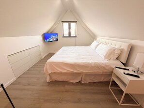 A bedroom with a bed, a TV mounted on the wall, a window with blinds, and a bedside table with a lamp and remote controls. - Downtown Loft Walk to Beach CasaAmarilla302 (Oranjestad)