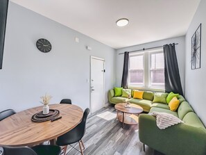 En moderne stue med en grøn sofa, et træspisebord og et ur på væggen.