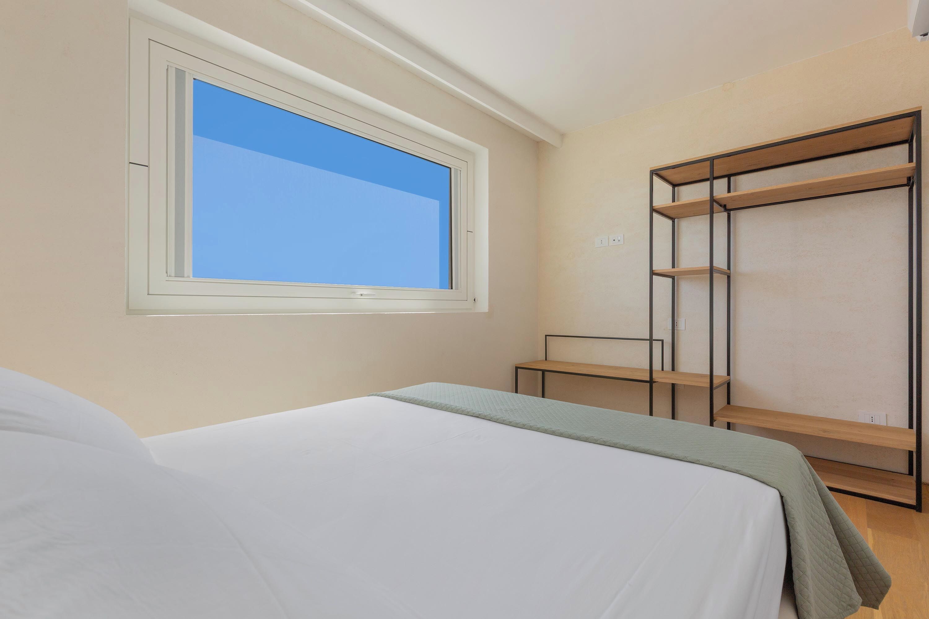 A bedroom with a bed, a window, a wardrobe, and a small table.