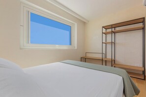 Un dormitorio con cama, ventana, armario y una mesita.