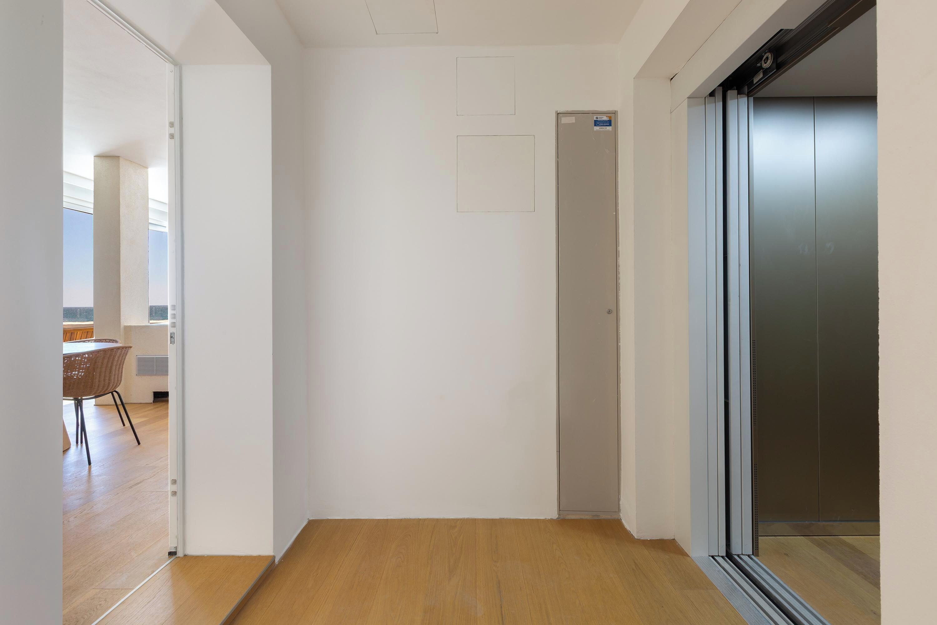 A hallway with a wooden floor, a door, and an elevator.