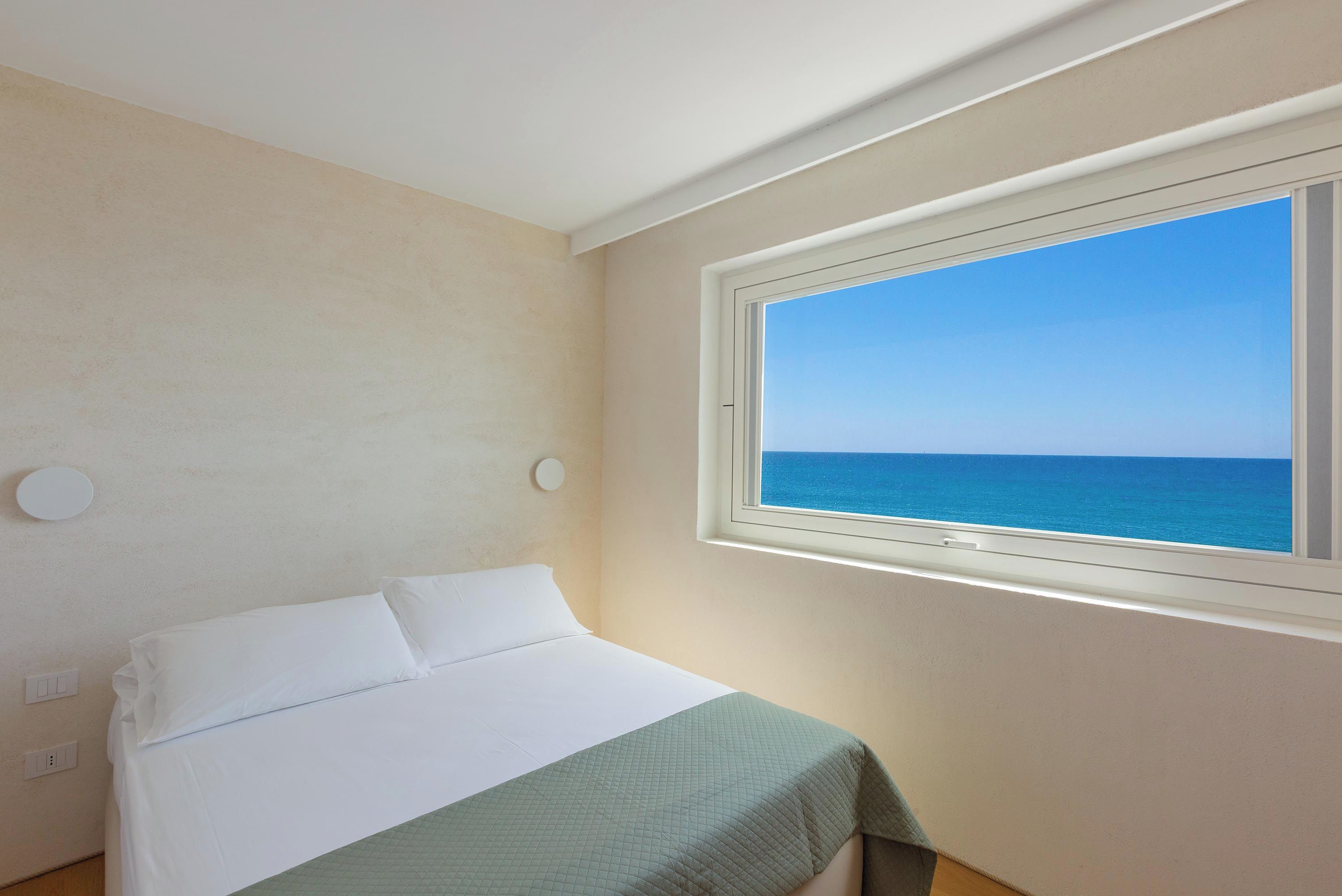 A bedroom with a bed, a window with a view of the sea, and a light switch on the wall.