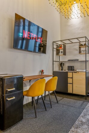A modern office space with a flat-screen TV displaying 'NETFLIX', a wooden desk, two yellow chairs, a black filing cabinet, and a kitchenette area. - Studio at Karmelitermarkt | Self-Check-In | Old Town Within Walking Distance (Wien)