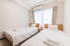 Et hotelværelse med to senge, et vindue med gardiner, et klimaanlæg og et natbord med et ur.