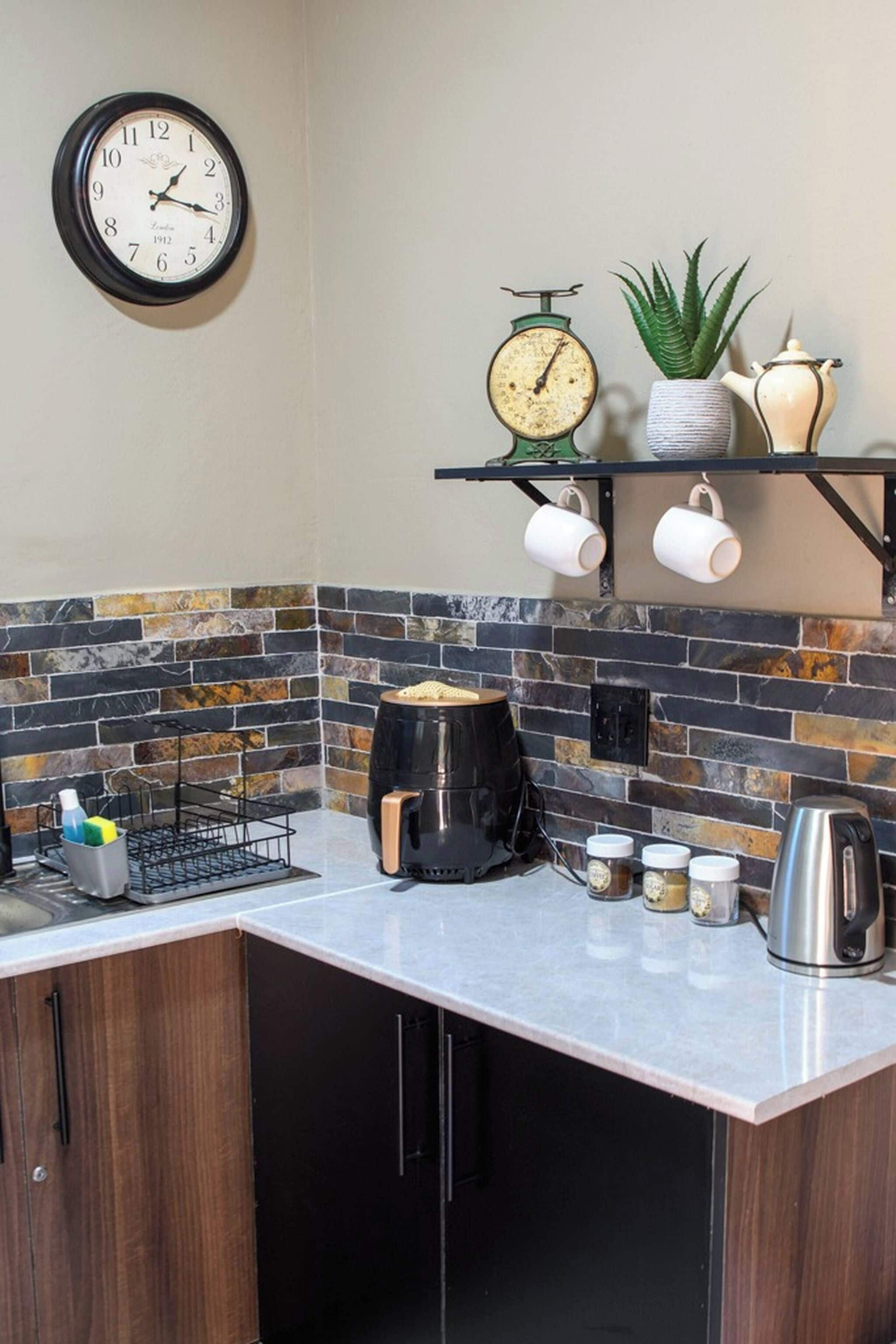 A kitchen with a clock, a scale, a plant, and a coffee maker.