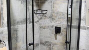 A walk-in shower with a glass door, checkered floor tiles, and a towel rack to the left.