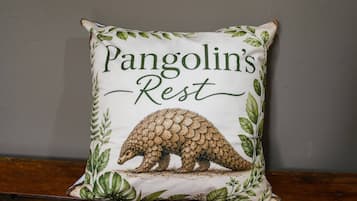 Een vierkant kussen met een pangolin-illustratie en de tekst 'Pangolin's Rest' op een effen muur.