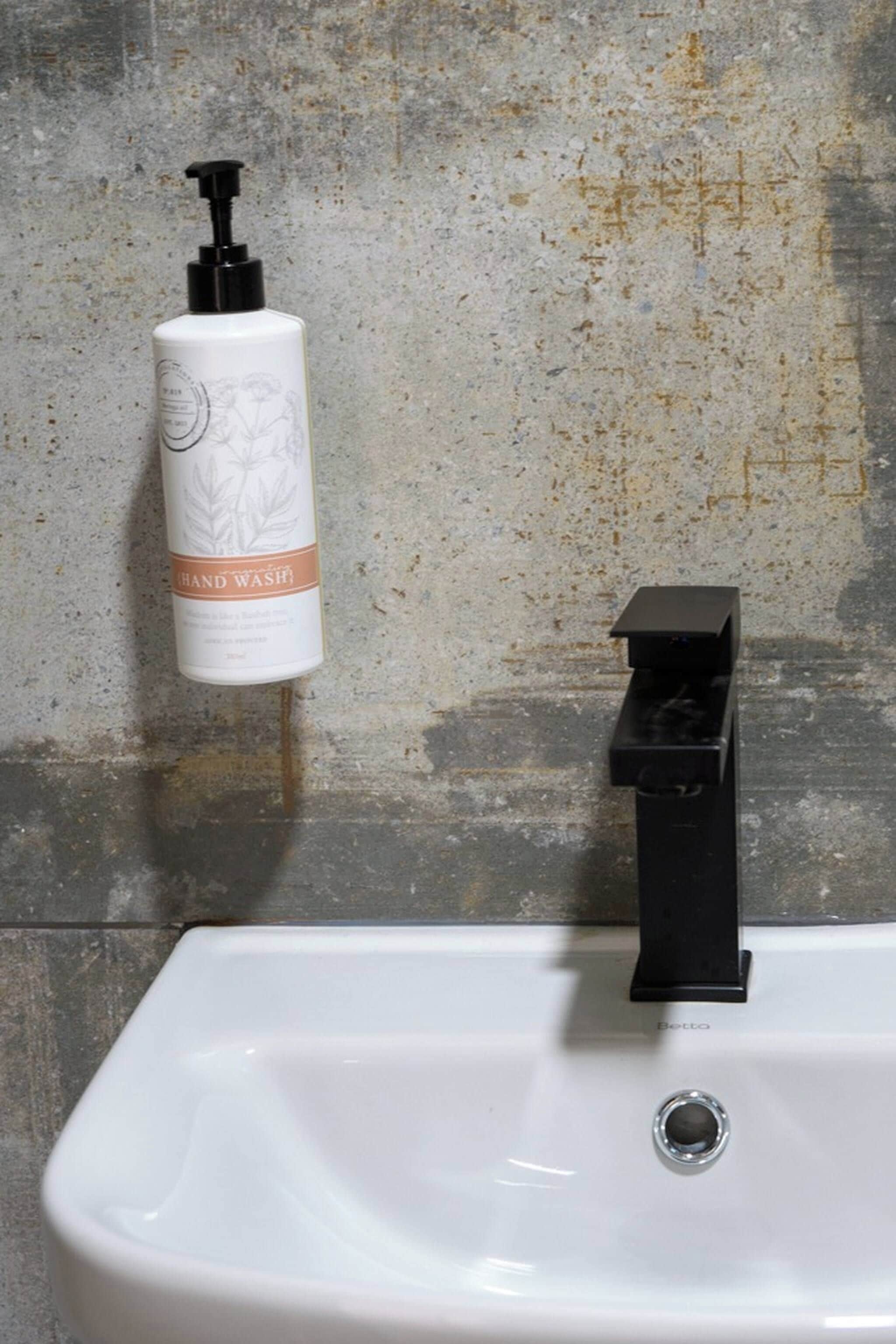 A bathroom sink with a black faucet and a hand wash dispenser on the wall.