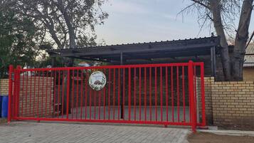 Una entrada con reja metálica roja, pared de ladrillo y zona cubierta con techo.