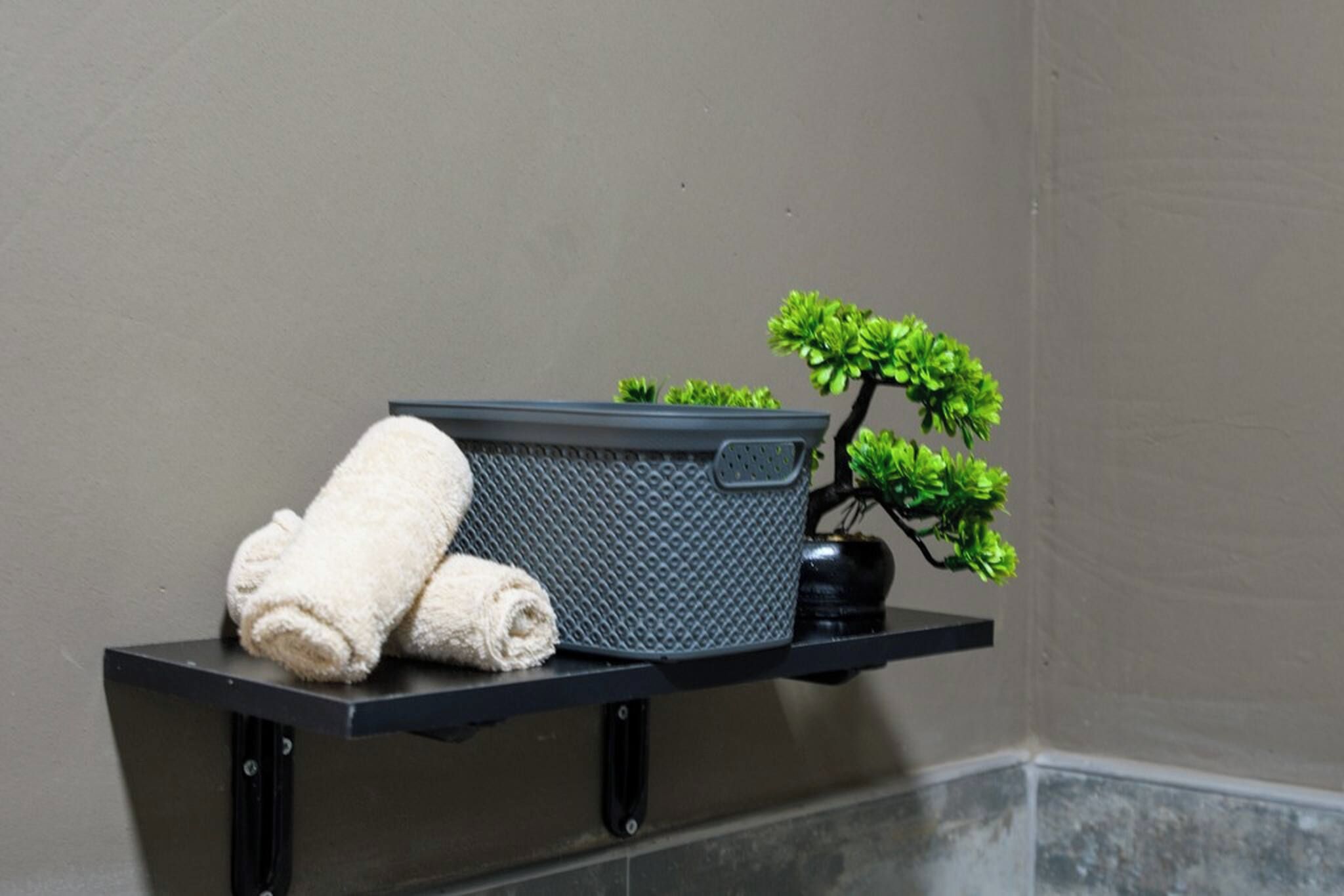 Una toalla sobre un estante, una cesta con textura y una pequeña planta en maceta.