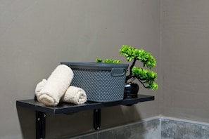 Una toalla sobre un estante, una cesta con textura y una pequeña planta en maceta.