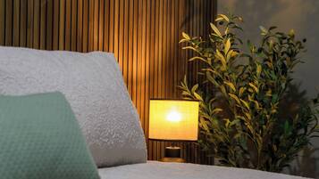 Un lit avec des oreillers, une lampe de chevet et une plante en pot, dans une pièce aux murs lambrissés.
