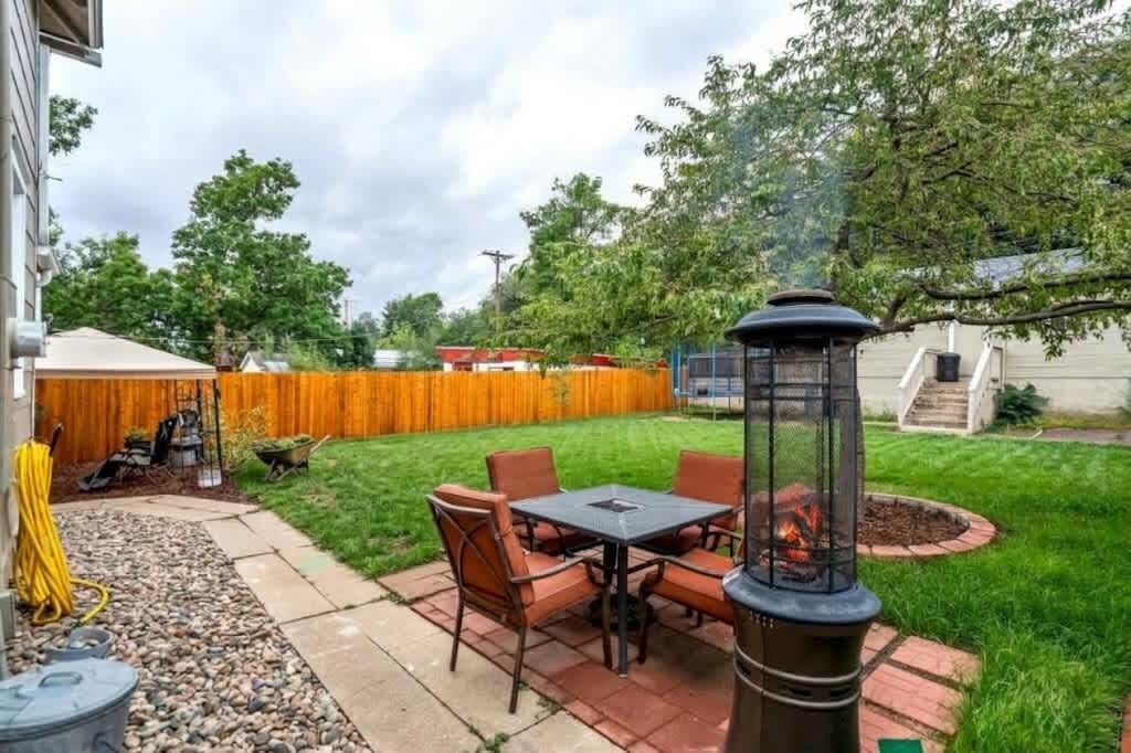 A patio with a table and chairs, a fire pit, and a wooden fence in the background.