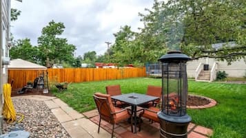 A patio with a table and chairs, a fire pit, and a wooden fence in the background.