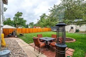 A patio with a table and chairs, a fire pit, and a wooden fence in the background. - Chestnut Hill! Downtown Historic Home w Hot Tub (Colorado Springs)