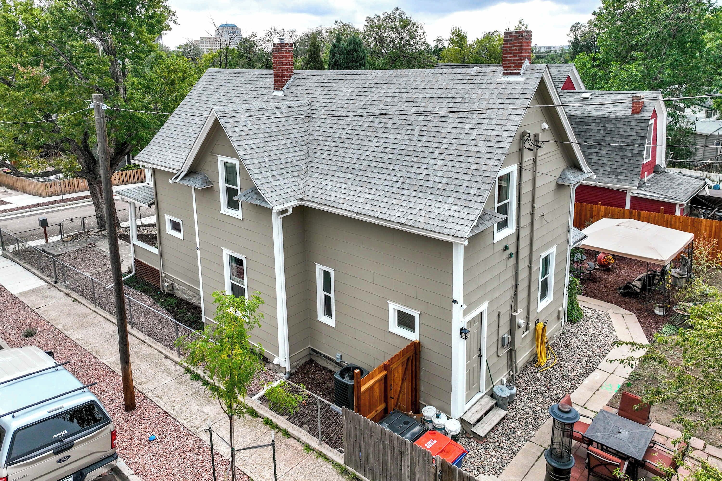 A two-story house with a grey roof, a fenced yard, and a parked vehicle.