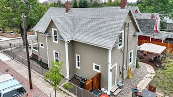 A two-story house with a grey roof, a fenced yard, and a parked vehicle.