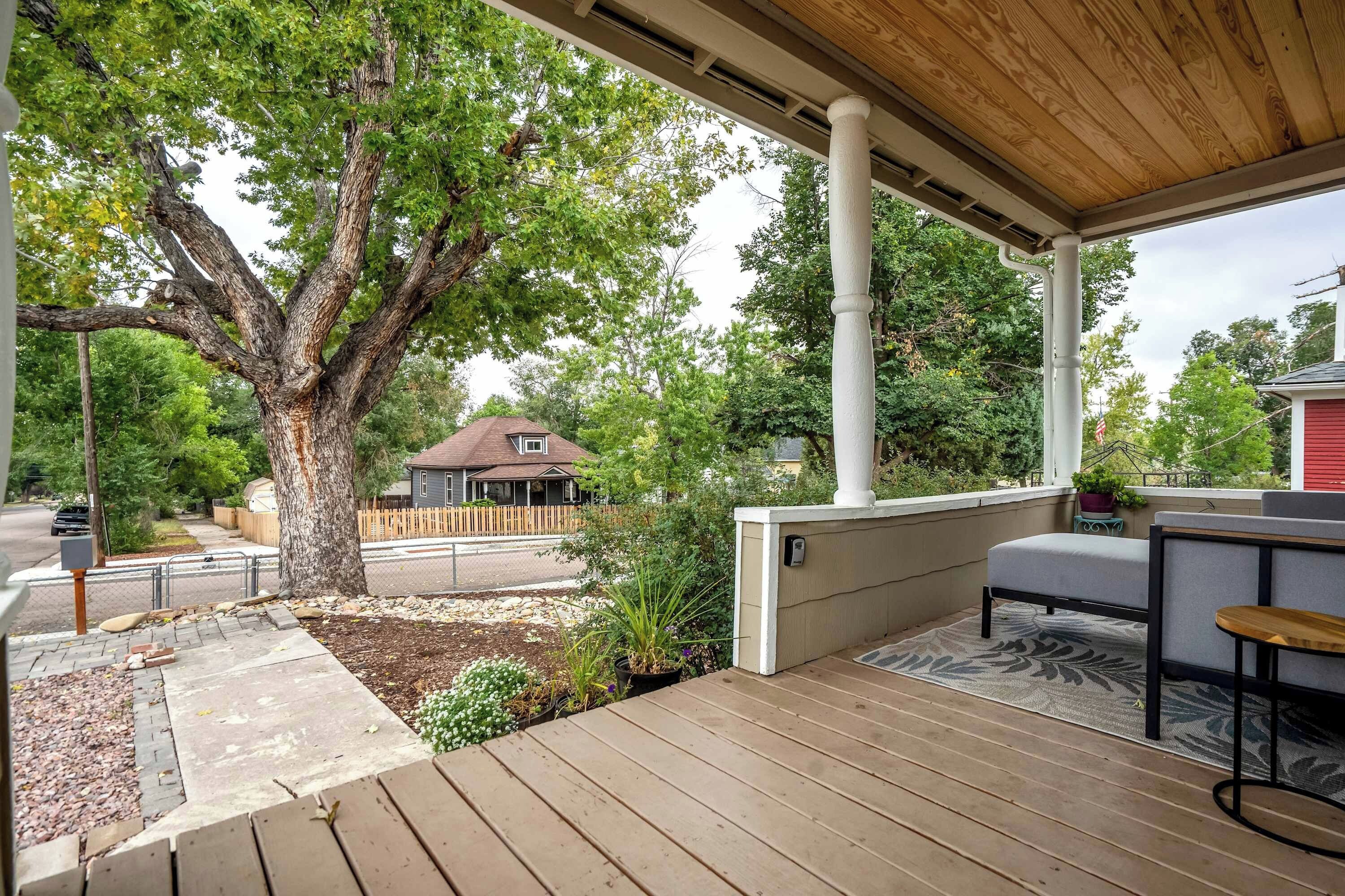 A wooden deck with a built-in seating area, a tree, and a view of a residential street.